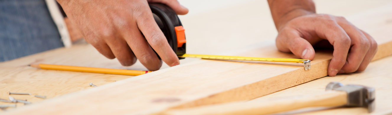 A student measures a board laying on a workbench with a hammer and nails laying nearby.