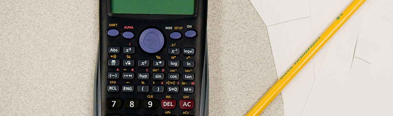 A scientific calculator, a yellow pencil, and sheets of paper on a table surface.