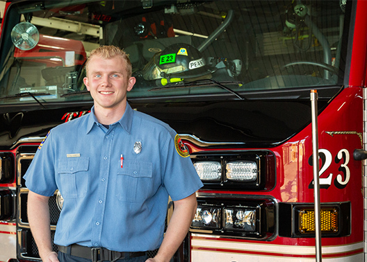 Alumnus smiles in firefighter uniform in front of truck