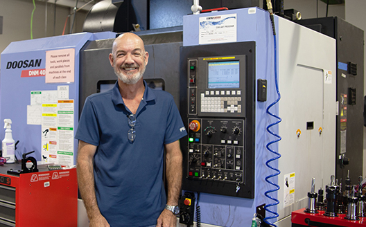 Instructor smiles in front of CNC machine