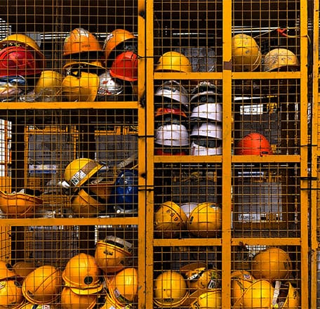 Hardhats stacked in metal storage containers.