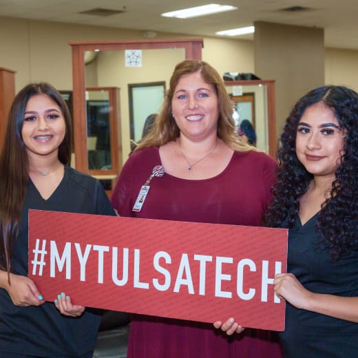 An smiling instructor and two students hold a #MyTulsaTech sign