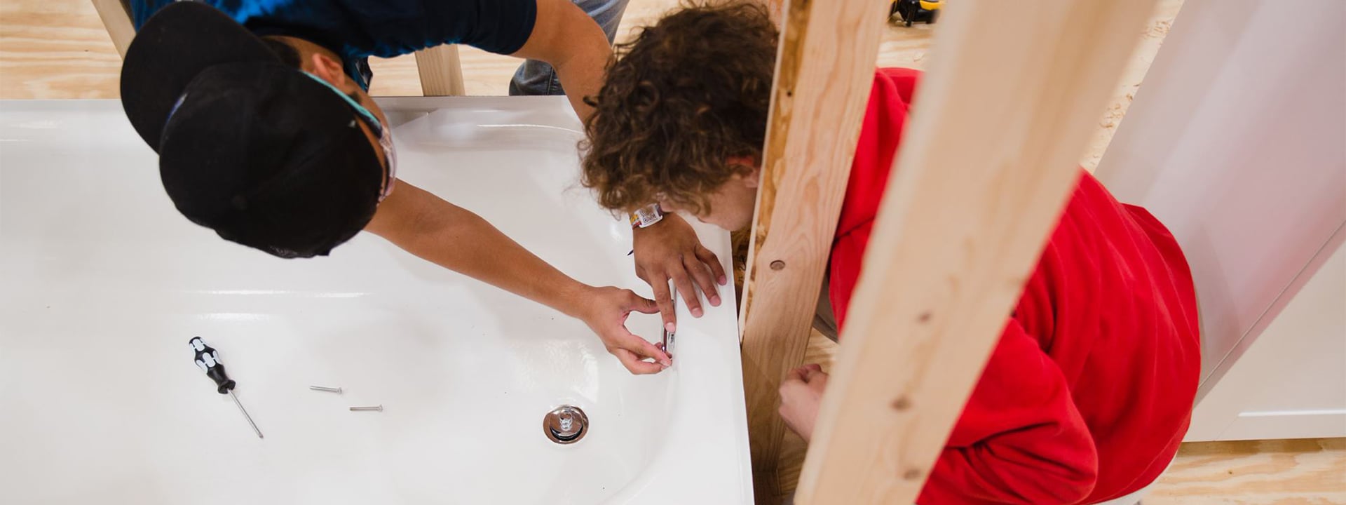 Two students work to install plumbing for a tub