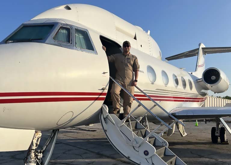 Aviation Maintenance graduate Jesse Moore stands in the boarding door of an aircraft on a sunny day.