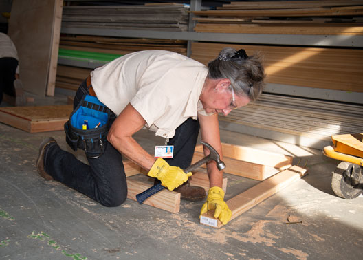 Carpentry Student Sandra Holloway kneels on floor while hammering nails