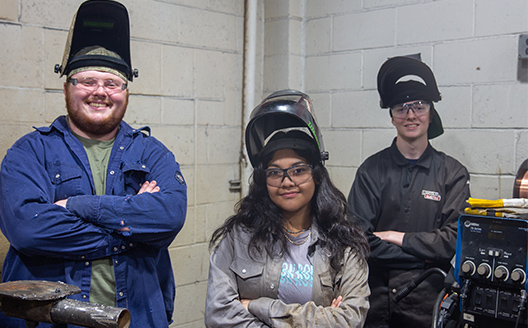 three student welders smiling at the camera