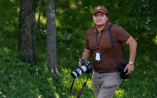 Photography graduate Victor Lopez pictured in a wooded area with cameras