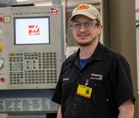 Tulsa Tech student, Zach, stands next to machining equipment